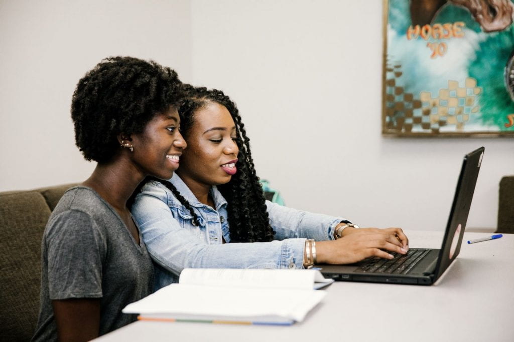 two students seated closely together working on a lap top 